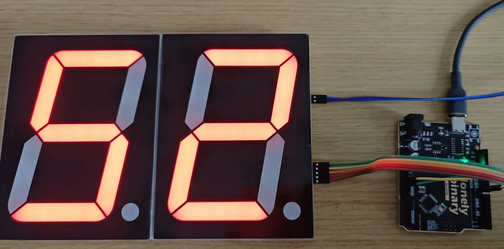 Two chained 4-inch modules seen from the front with their digits lit red, sitting flush against each other so the two digits read as one number, with five ribbon wires running from the right-hand module to a black Arduino-compatible board.