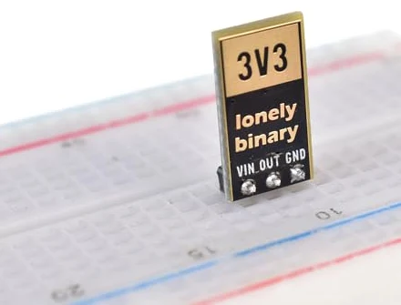 A 3.3 volt regulator board standing upright in a white breadboard, seen from the back: 3V3 printed in a gold box, the lonely binary logo below, and VIN, OUT, GND above the three pins that go into three rows.