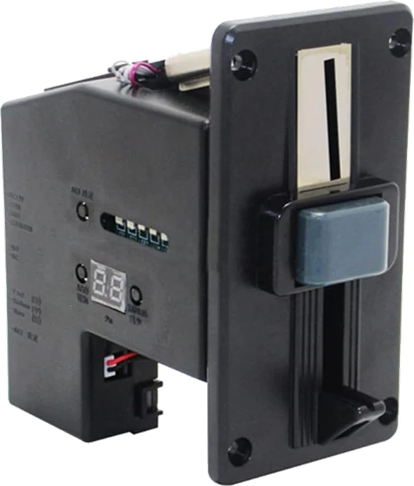 The coin acceptor at an angle: a black plastic body about the size of a paperback behind a flat front plate with a vertical coin slot, a hinged reject lever below it, four bolt holes at the corners of the plate, and on the side a two-digit red display, three round buttons and a row of small switches.