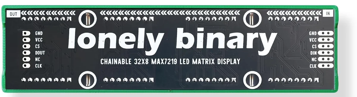 The back of the green 32x8 board: a black PCB printed lonely binary and CHAINABLE 32X8 MAX7219 LED MATRIX DISPLAY, with a six-pad header at the right marked IN and labelled GND, VCC, CS, DIN, NC, CLK downwards, and a matching six-pad header at the left marked OUT and labelled GND, VCC, CS, DOUT, NC, CLK.