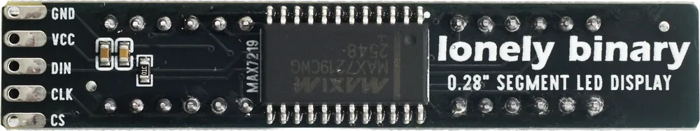 The solder side of the driver board, a long thin black PCB. Five oval pads down the left edge are printed GND, VCC, DIN, CLK and CS. A twenty-four pin wide SO chip marked MAXIM MAX7219CWG sits in the middle with a twelve-pad display footprint in two rows of six either side of it, and two capacitors and one chip resistor sit near the pads.