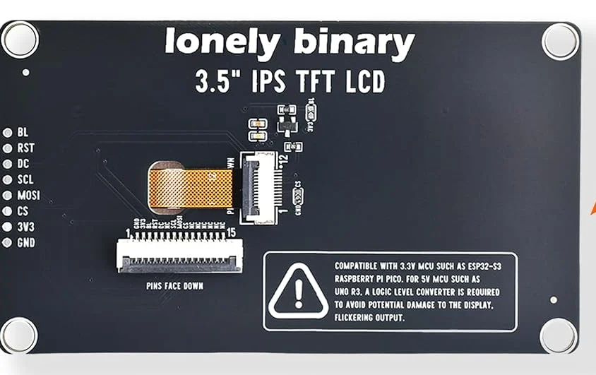 The back of the 3.5 inch display board, black with white silkscreen. Along the left edge, eight round pads are labelled from the top BL, RST, DC, SCL, MOSI, CS, 3V3 and GND. The centre carries lonely binary and 3.5 inch IPS TFT LCD in large letters, a fifteen-way FPC socket numbered 1 to 15 marked PINS FACE DOWN, the orange flex tail from the glass folded into a second connector, and a printed warning that the board is for 3.3 volt microcontrollers and that a 5 volt board needs a level converter.